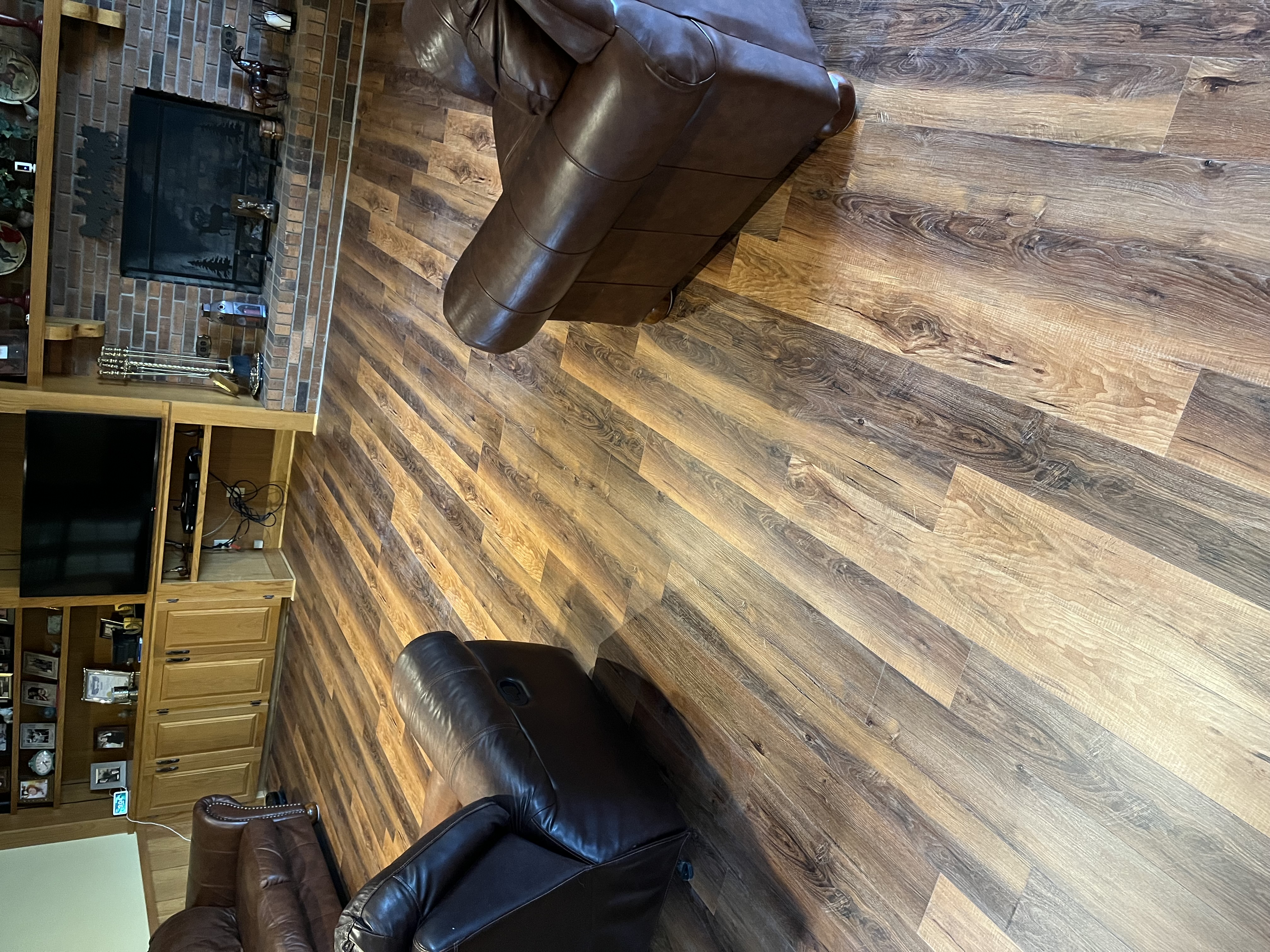 Luxury vinyl plank flooring installed in a living room with leather furniture and brick fireplace